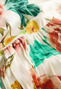 Tissu floral en matériau doux et léger. Présente des fleurs roses, jaunes et vertes sur un fond blanc avec des détails de texture froncés.