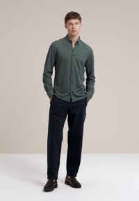 Cămașă verde Închis cu guler button-down, mâneci lungi și textură subtilă. Asortată cu pantaloni negri închis și mocasini negri.