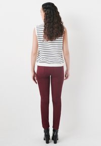 Top sin mangas, blanco con rayas navy; pantalones ajustados color burdeos; modelo lleva botas de tacón negras; mostrado desde atrás sobre un fondo blanco.