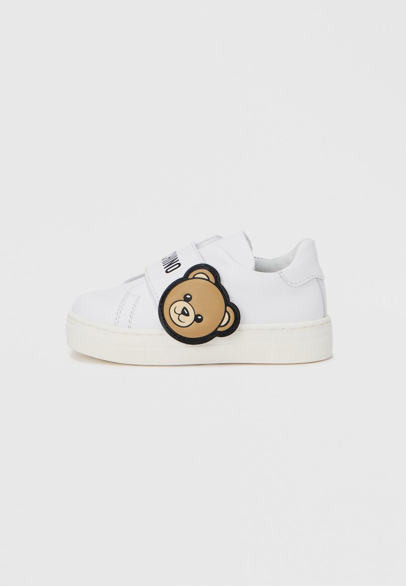 Λευκά αθλητικά παπούτσια με λείο δερμάτινο φινίρισμα. Διαθέτουν στρογγυλό κέντημα αρκούδας και μαύρο λουρί. Λαστιχένια σόλα, σχεδιασμός χαμηλού ύψους, casual εμφάνιση.