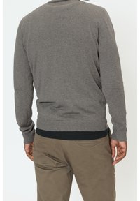 Pull gris en maille avec manches longues et poignets côtelés, associé à un pantalon marron clair. Le pull présente un col rond et une coupe décontractée.