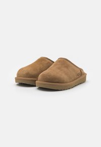Zoccoli in suede marrone con punta arrotondata e superficie testurizzata. Presentano una suola in gomma con piccole scanalature per la trazione.