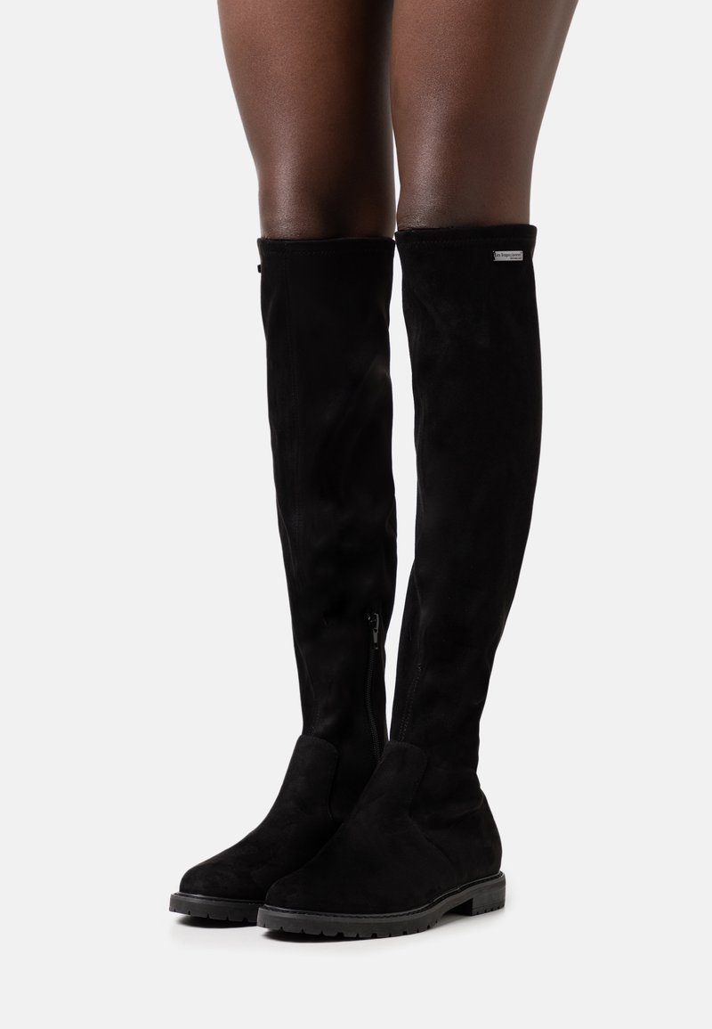 Botas negras por encima de la rodilla hechas de suave ante, con cremallera lateral, suela plana y una textura lisa, con un diseño aerodinámico.