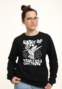 Felpa nera con grafica bianca che presenta un colibrì, foglie tropicali e testo: "SIMPLE LIFE TROPICAL." Vestibilità comoda, maniche lunghe.