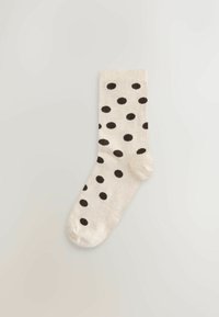 Smėlio spalvos kojinė juodais taškeliais, su siūluota tekstūra ir sustiprintais pirštais. Kulkšnies ilgio dizainas, tinkamas kasdieniam dėvėjimui.