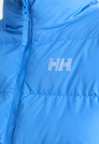 Ljusblå isolerad jacka med blixtlås, med en slät textur och en vit logotyp på bröstet.