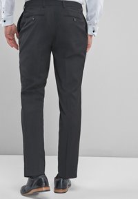 Pantalons habillés noirs à coupe ajustée, dotés de deux poches arrière, en tissu lisse et à la finition soignée. Associés à des chaussures habillées noires.