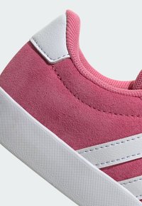 Zapatillas de ante rosa con una suela de goma texturizada blanca, con detalles en piel blanca y costuras a lo largo de los lados.