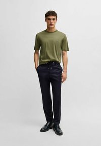 Olivgrön bomullströja med rund halsringning, kombinerad med marinblå byxor med dragsko. Svarta snörskor fulländar outfiten.