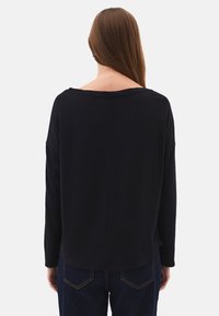 Zwarte longsleeve met een wijde halslijn en een losse pasvorm. Zachte textuur, minimalistisch ontwerp, en gecombineerd met donkerblauwe jeans.