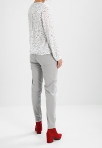 Maglietta bianca a maniche lunghe con macro macchie nere, abbinata a pantaloni grigi e stivali rossi con tacco alto. Tessuto morbido, vestibilità comoda e design semplice.