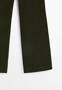 Jambes de pantalons en velours côtelé vert foncé avec ourlets droits sur fond blanc, montrant la texture et les détails de la couleur du tissu.