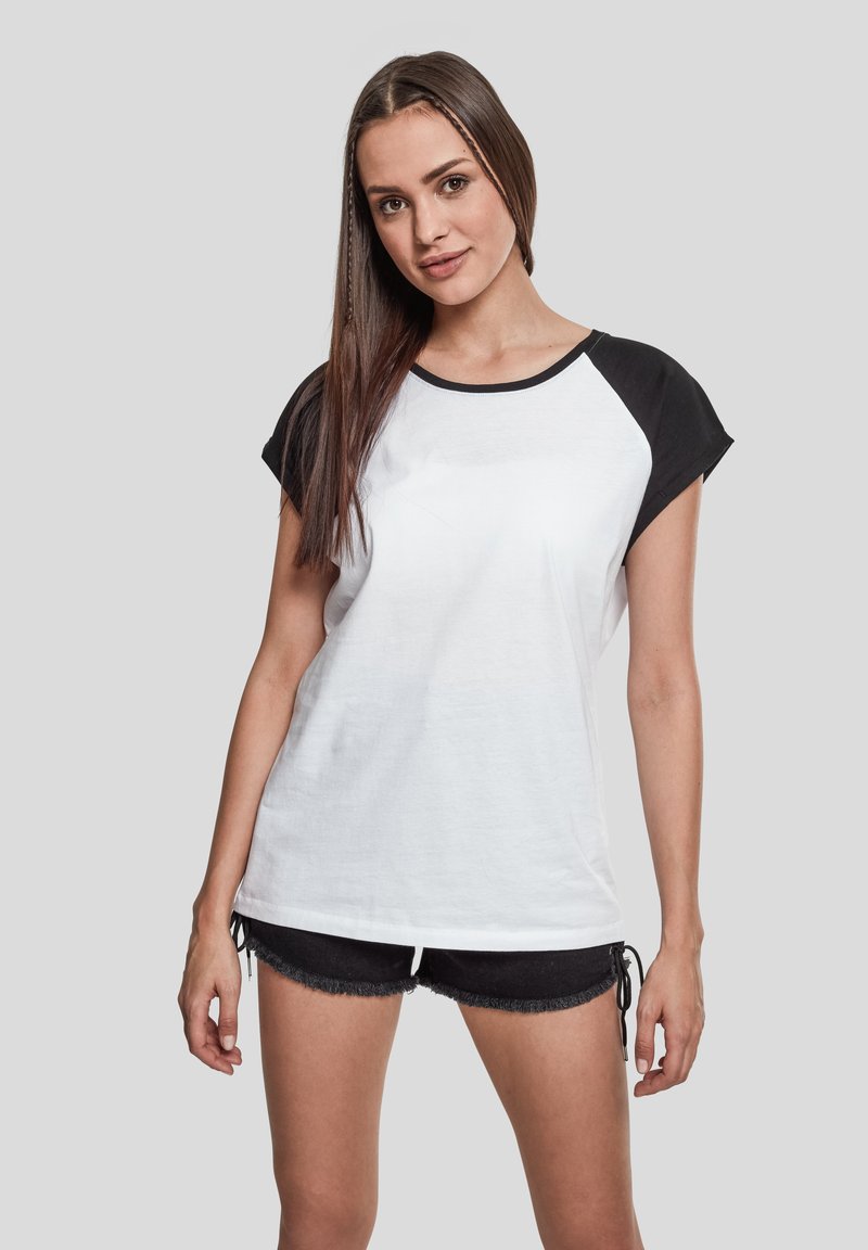 Camiseta blanca de manga corta con detalles en negro en las mangas y el escote, que presenta un corte holgado y una textura suave de algodón.