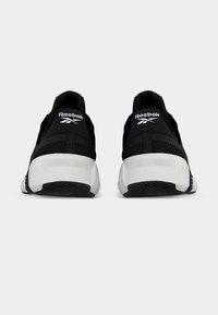 Ασπρόμαυρα αθλητικά παπούτσια Reebok, εμφανιζόμενα από πίσω, με χοντρές λευκές σόλες και μαύρα κολάρα φτέρνας με το λογότυπο.