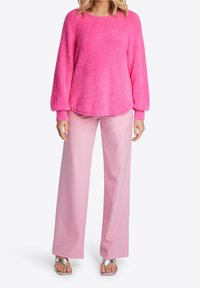Maglione fucsia morbido con maniche lunghe, abbinato a pantaloni larghi rosa chiaro e sandali con tacco argentati.
