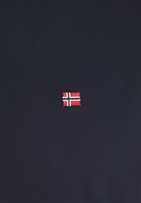 Mörkblå bomullströja med en liten broderad norsk flagga på vänster sida, med detaljer i rött, vitt och blått.
