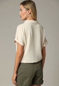 Crème, gestructureerd, kortmouwig shirt met een kraag, gecombineerd met olijfgroene shorts met opgerolde manchetten en achterzakken.