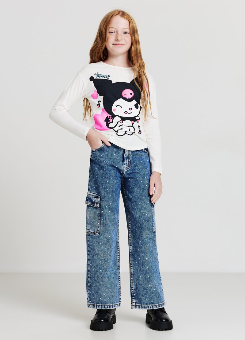 Chemise blanche à manches longues avec un graphique cartoon coloré, assortie à un pantalon cargo large en denim bleu avec poches latérales et détails tachetés.