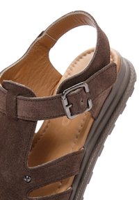 Sandalo in suede marrone con lati aperti, cinturino regolabile con fibbia e soletta imbottita e testurizzata, dotata di suola grigia resistente.