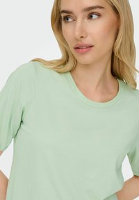 Lys grøn, kortærmet t-shirt med rund halsudskæring, fremstillet af blødt stof. Glat tekstur, enkelt design, ingen synlige mønstre eller accenter.