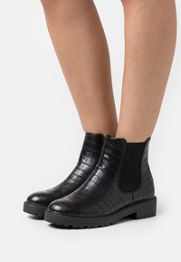 Botas negras de tobillo con un estampado texturizado de cocodrilo, paneles laterales elásticos y una suela de goma gruesa. Diseño de punta redondeada para mayor comodidad.