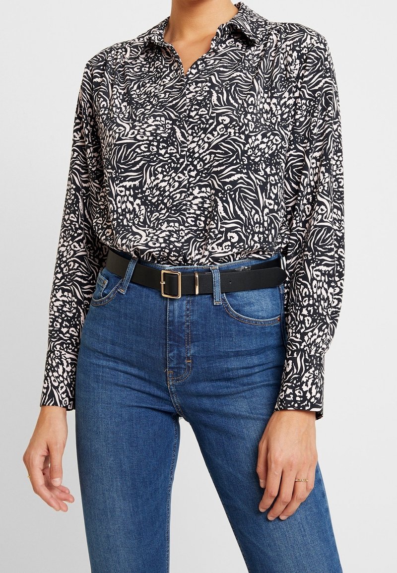 Black and white patterned long-sleeve shirt with a collar, worn with high-waisted blue jeans and a black belt featuring a gold buckle.