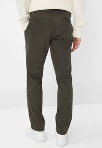 Chino in cotone verde oliva con taglio dritto, dotati di tasche posteriori e dettagli di cucitura discreti, abbinati a sneakers bianche.