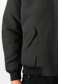 Schwarze Bomberjacke mit glatter Außenseite, gerippten Bündchen, Reißverschluss und einer Seitentasche in einem sauberen, minimalistischen Design.