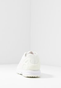 Vit sportskor med en strukturerad mesh-ovandel, lätt design, rosa detaljer och en solid gummisula. Har en logotyp på sidan.