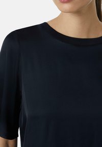 Navyblaues Kurzarmoberteil mit einer glatten, weichen Textur und einem runden Ausschnitt, das über einen subtilen Glanz und einen gerippten Saum am Kragen verfügt.