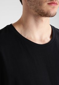 Camiseta de algodón negra con cuello redondo, mangas cortas y textura suave. Sin patrones ni logotipos visibles. Vista de cerca.