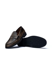 Mocassins en cuir marron avec une finition lisse, dotés d'une sangle décorative, de coutures, et d'une semelle en caoutchouc noir texturée.