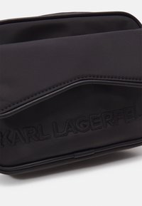 Pochette rettangolare nera con testo in rilievo "KARL LAGERFELD" e dettagli cuciti eleganti su uno sfondo bianco.