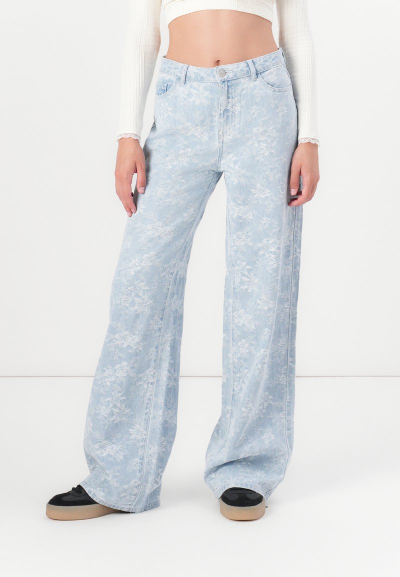Lichtblauwe wijde jeans met een bloemenpatroon, gemaakt van denim, met een hoge taille en traditionele zakdetails. Zwarte schoenen maken de look compleet.