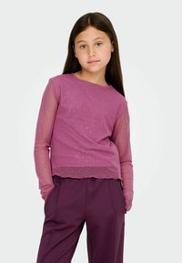 Long-sleeve top in a magenta color with a sheer, dotted overlay. Features a classic crew neckline and relaxed fit. Paired with dark purple trousers.