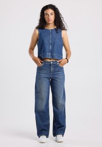 Blue denim cropped tank top with sleeveless design, paired with high-waisted, wide-leg jeans. White sneakers complete the outfit.