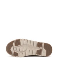 Suola di una scarpa in beige chiaro con motivi testurizzati, dotata di tacco arrotondato e sezioni di accenti marroni scuri. Il nome del marchio è visibile.