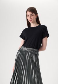 Un tricou scurt negru, cu mânecă scurtă, asortat cu o fustă plisată metalică argintie, cu talie elastică și o strălucire verticală.