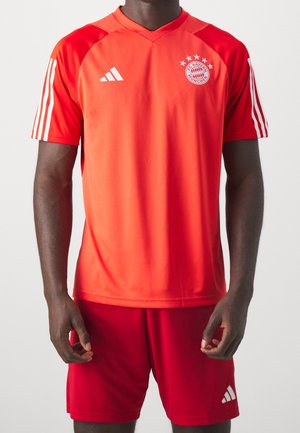Man wearing bright red FC Bayern Munich soccer jersey and matching shorts with white Adidas logos and stripes on sleeves.