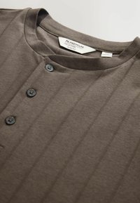 Tumedat hallid henleysi särgid, mis on valmistatud pehmest kangast, millel on peened püstised triibud, lühike krae ja kolm esit nööpi. Sildi osa on nähtav krae sees.