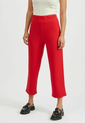 Pantalons rouges courts en tissu lisse avec une taille élastique, associés à des mocassins noirs avec une semelle épaisse et des détails en métal.