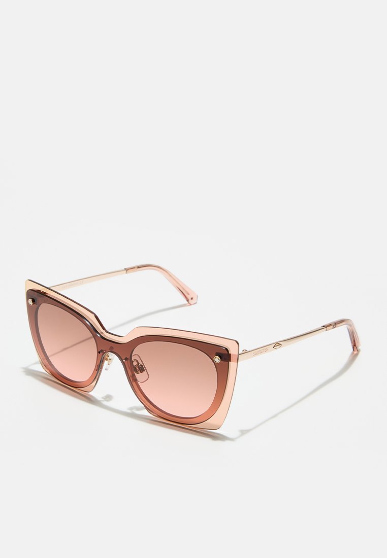 Roze oversized zonnebril met een geometrische cat-eye vorm, gemaakt van transparant plastic. Gradient lenzen en metalen accenten op de pootjes.