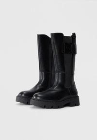 Black leather knee-high boots with a textured finish, side zipper, and a wide, chunky rubber sole. Features a buckle accent on the upper.