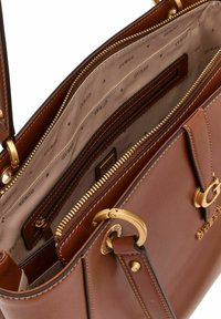 Bolso de mano de piel sintética marrón con un compartimento principal con cremallera, herrajes en tono dorado y forro interior texturizado con un patrón de logo.