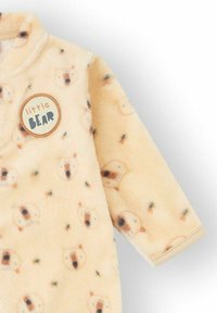 Mono beige suave para bebé con un patrón de pequeñas caras de oso y un parche redondo en el pecho que dice "pequeño OSO".