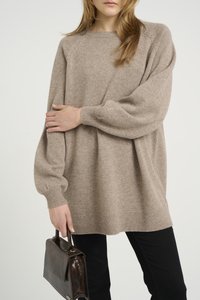 Beige, túlságosan nagy pulóver, raglán ujjal, bordázott mandzsettával és szegéllyel. Fekete nadrággal és egy kis barna bőrtáskával párosítva.