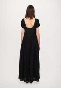 Juoda maksi suknelė su prigludusia smulkinta liemene, trumpomis rankovėmis, plačia platėjanti sijona ir scalloped eyelet detalėmis apatinėje dalyje. Atvira nugara.