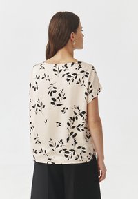 Short-sleeve blouse in light beige with black leaf pattern. Soft, lightweight fabric with a relaxed fit and rounded neckline, visible from the back.