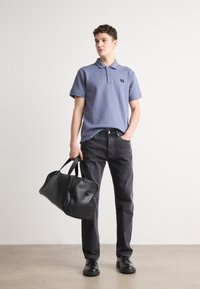 Sac de sport en cuir noir, polo bleu clair avec col, jean gris foncé et chaussures noires. Textures lisses et coupe décontractée.