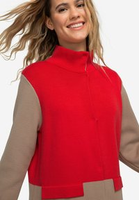 Maglione con blocchi di colore rosso e beige, colletto alto, tessuto a maglia testurizzato e dettaglio dei bottoni sulla parte anteriore.
